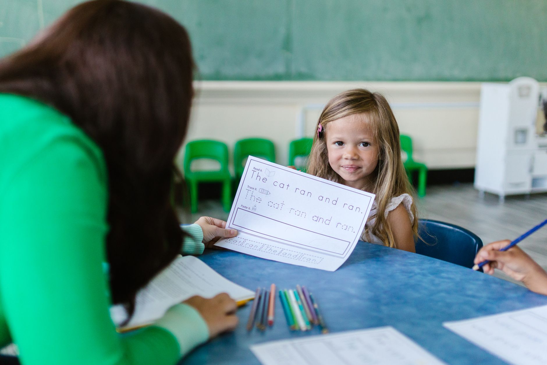 A clinician and a child at a table working through a printed word list with a pencil.